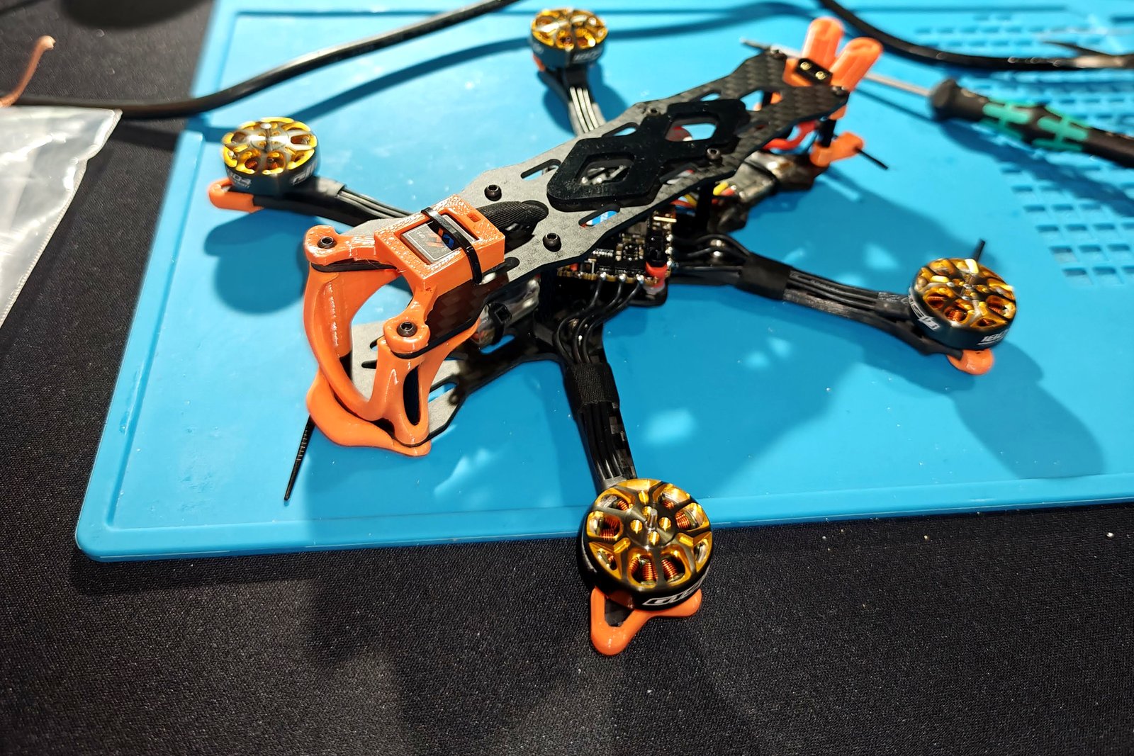 Mikro dron FPV z pomarańczowymi wydrukami TPU na macie warsztatowej